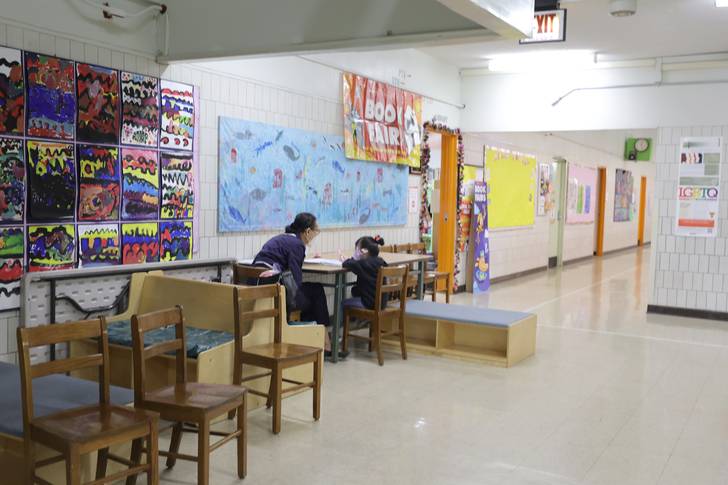 Photo of a a pre-K student sitting with a teacher outside a classroom in Manhattan.